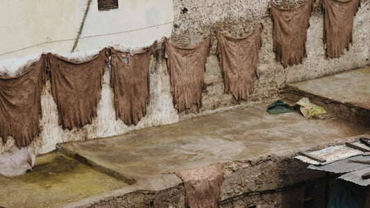 Traditional leather tanning process with animal hides hanging to dry on a stone wall in an outdoor tannery, showcasing the artisanal methods of leather production.