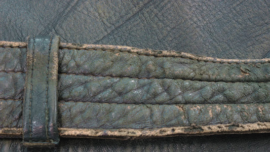 A close-up view of an aged and worn piece of leather, showcasing visible signs of wear and tear. The leather surface has a rough texture with faded colors, creases, and scuffs, indicating prolonged use and exposure to elements. 